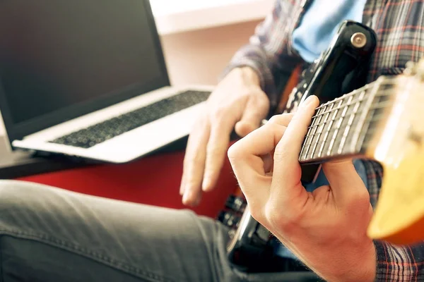 Случайно одетый молодой человек с гитарой играет песни в комнате дома. Концепция онлайн уроков гитары. Мужчина-гитарист, практикующий рукоятки аккордов . — стоковое фото