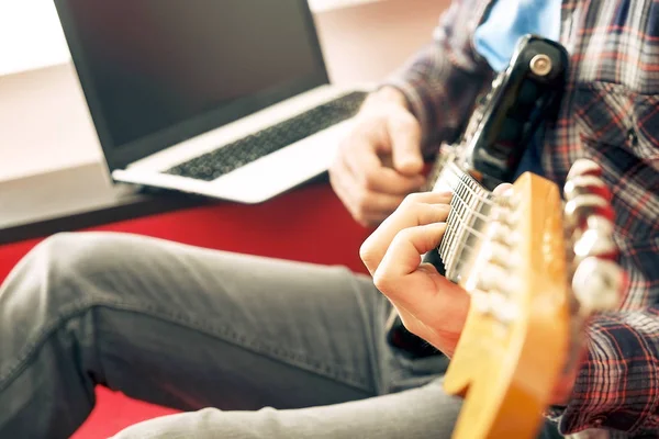 Случайно одетый молодой человек с гитарой играет песни в комнате дома. Концепция онлайн уроков гитары. Мужчина-гитарист, практикующий рукоятки аккордов . — стоковое фото