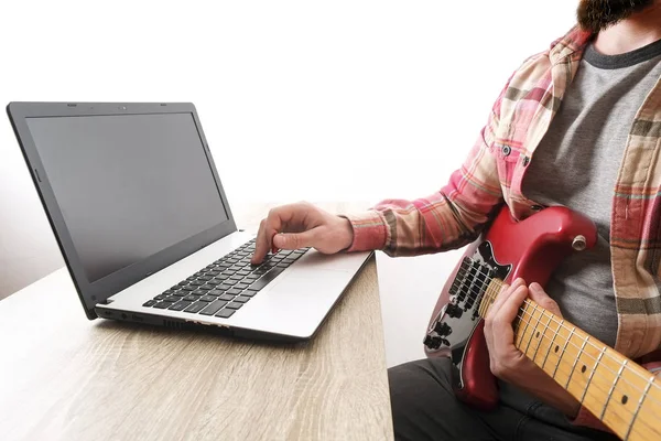 Niedbale ubrany broda młody człowiek z gitara odtwarzanie utworów w pokoju w domu. Laptop na stole. Koncepcja lekcje online na gitarze. Gitarzysta mężczyzn praktykujących akord uchwyty. — Zdjęcie stockowe