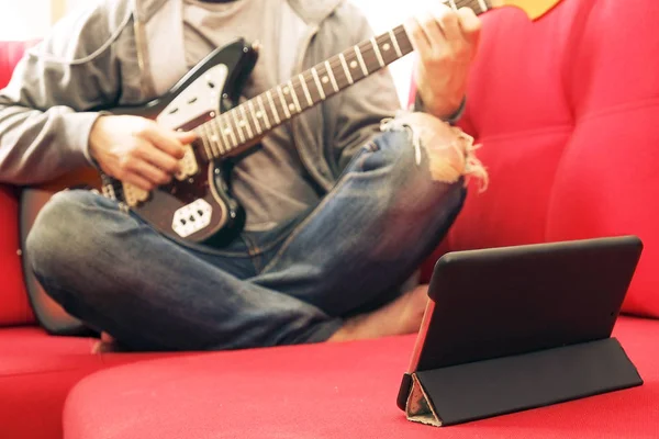 Lässig gekleideter junger Mann mit Gitarre, der zu Hause Lieder spielt. Online-Gitarrenunterricht Konzept. männlicher Gitarrist übt Akkordgriffe. — Stockfoto