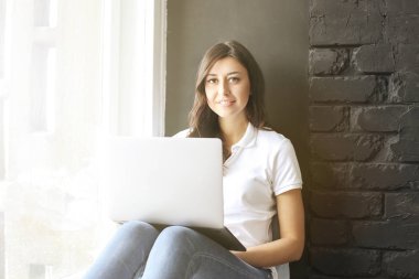 Pencere laptop w / mutlu bin yıllık kız. Dişler arasındaki diastema boşluğu olan kadın portresi. Güzel gülümseme. En az iç, siyah tuğla duvar arka plan, loft tarzı dokulu. Kopya alanı.