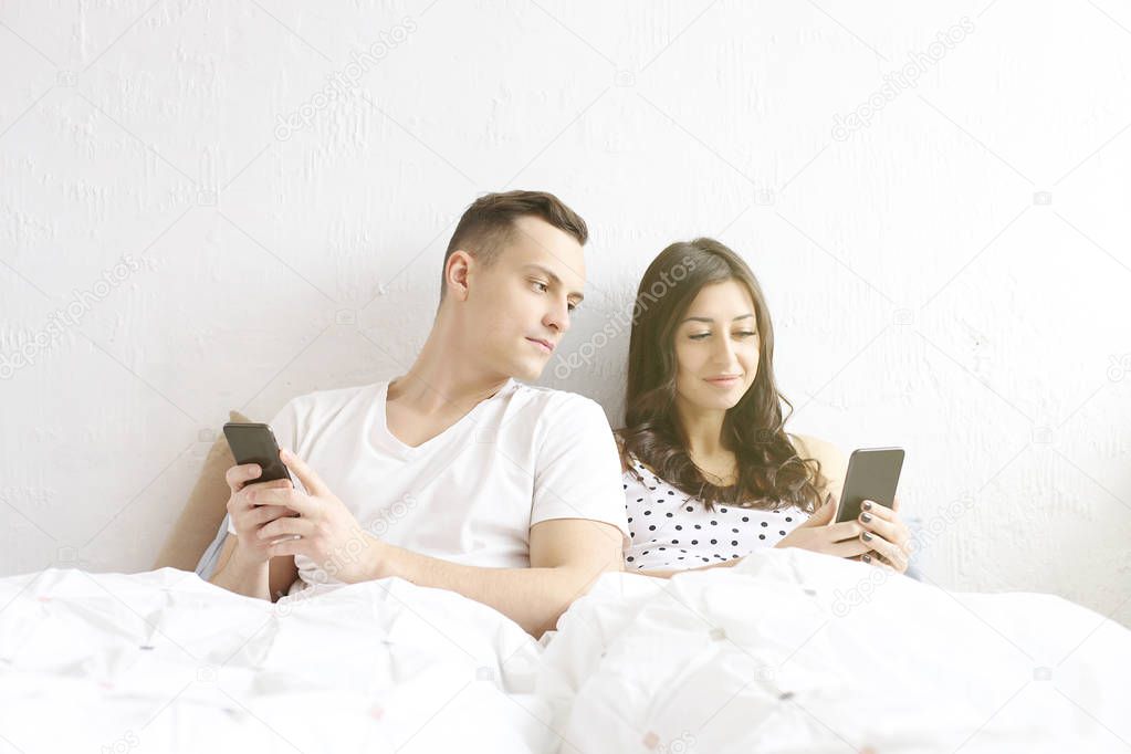 Jealous husband spying his wife mobile phone while she is reading a message. Technology & relationship concept. Modern romance troubles. Male and female online dating app. Swiping, browsing, surfing