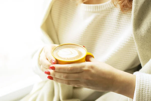 Concepto de pausa. Primer plano de las manos femeninas sosteniendo una taza amarilla de café capuchino con espuma de leche. Arte latte. Atractiva mujer joven hipster en la cafetería loft moderno restaurante . — Foto de Stock