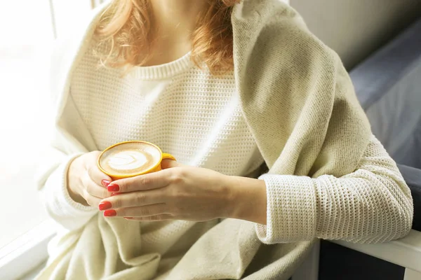 Concepto de pausa. Primer plano de las manos femeninas sosteniendo una taza amarilla de café capuchino con espuma de leche. Arte latte. Atractiva mujer joven hipster en la cafetería loft moderno restaurante . — Foto de Stock