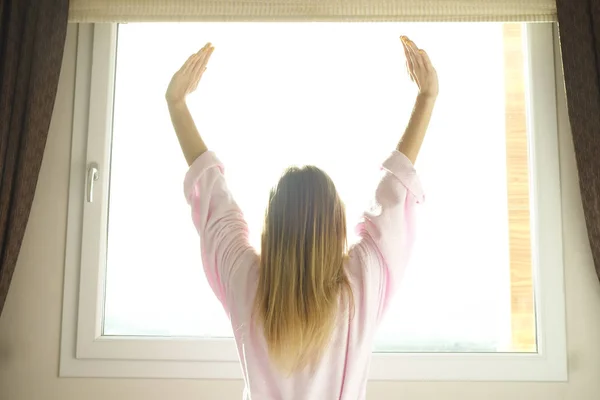 Großes, geräumiges Hotelzimmer voller Sonnenlicht und Sonnenstrahlen. optimistischer Start in den Tag. Blonde Frau gemütliche Kleidung zu Hause begrüßt den Morgen Tageslicht. neuer Tag neues Ich-Konzept. — Stockfoto