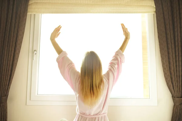 Gran habitación espaciosa de hotel llena de luz solar y rayos de sol. Comienzo optimista del día. Mujer rubia ropa de casa acogedora bienvenida a la luz del día por la mañana. Nuevo día nuevo concepto de mí . — Foto de Stock