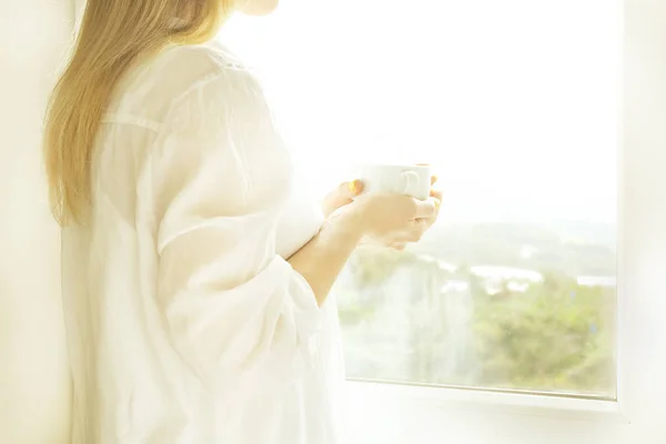 Big spacey hotel room full of sunlight and sun beams. Optimistic start of the day. Blond woman cozy home clothing welcoming the morning daylight. New day new me concept. — Stock Photo, Image