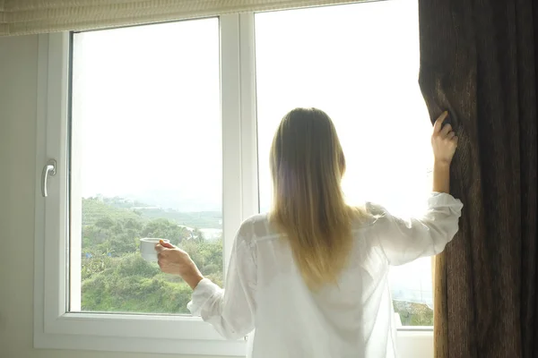 Großes, geräumiges Hotelzimmer voller Sonnenlicht und Sonnenstrahlen. optimistischer Start in den Tag. Blonde Frau gemütliche Kleidung zu Hause begrüßt den Morgen Tageslicht. neuer Tag neues Ich-Konzept. — Stockfoto