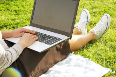 Onun dizüstü bilgisayarda ödev yeşil çim üzerinde oturan Üniversite öğrenci kız. Makale, eshopping, sosyal ağ üstünde onun pc defter yazma genç kadın park bloglama oturuyordu. kopya alanı.