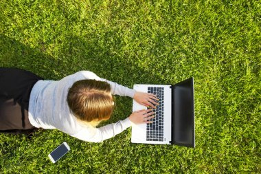 Onun dizüstü bilgisayarda ödev yeşil çim üzerinde oturan Üniversite öğrenci kız. Makale, eshopping, sosyal ağ üstünde onun pc defter yazma genç kadın park bloglama oturuyordu. kopya alanı.