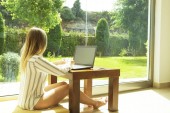 Szép csípő nő laza csíkos inget ül otthon, a személyi számítógép használata. Női író írt forgatókönyv otthon, nagy ablak, ivóvíz minőségű kávé. másol hely, háttér, közelről