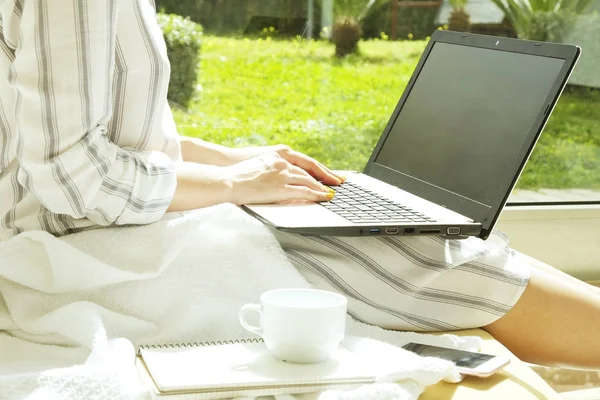 Женщина-хипстер в свободной полосатой рубашке сидит дома, используя персональный компьютер. Писательница пишет сценарий дома, у большого окна, пьет кофе. пространство для копирования, фон, крупный план — стоковое фото