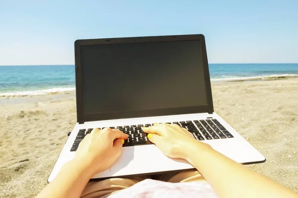 Young blonde hair woman working on laptop at the beach on sunny day. Close up of female hands typing on white notebook computer laptop, blogging, copywriting. Close up, copy space.