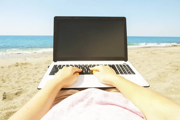 Young blonde hair woman working on laptop at the beach on sunny day. Close up of female hands typing on white notebook computer laptop, blogging, copywriting. Close up, copy space.