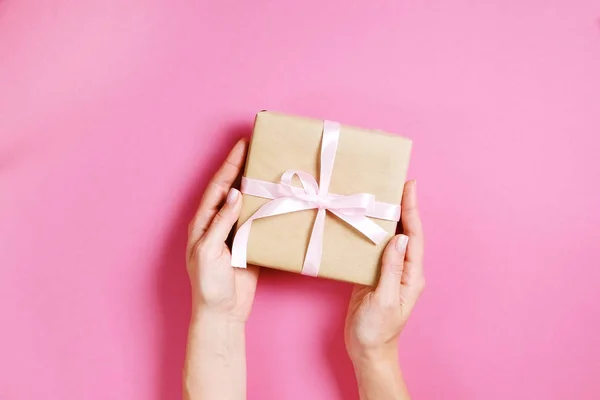 Primer plano de las manos femeninas sosteniendo regalo de cumpleaños en envoltura de papel artesanal vintage. Composición femenina con presente en los brazos de la mujer . — Foto de Stock