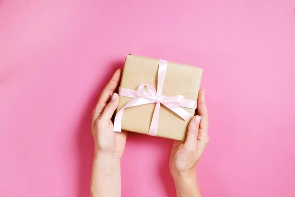 Close up van vrouwelijke handen met verjaardagsgift in vintage ambachtelijke papier verpakking. Femenine samenstelling met heden in de armen van de vrouw. — Stockfoto