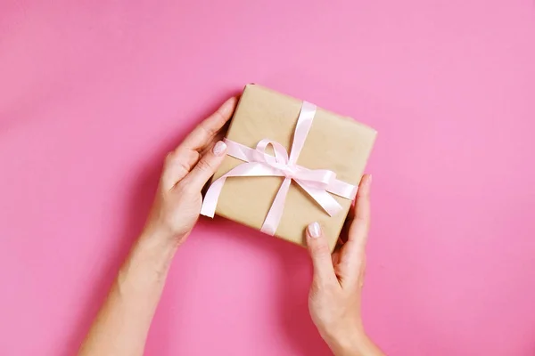 Primer plano de las manos femeninas sosteniendo regalo de cumpleaños en envoltura de papel artesanal vintage. Composición femenina con presente en los brazos de la mujer . — Foto de Stock