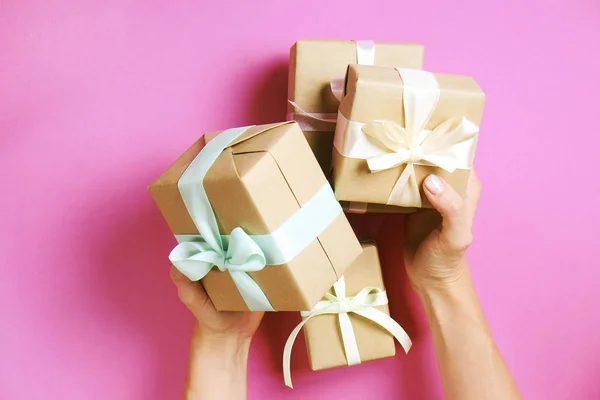 Mujer joven sosteniendo manojo de regalos envueltos en papel de regalo artesanal hecho a mano envoltura, lazo de satén. Manos femeninas, caja de regalo simple, envoltura, envoltura de regalo, cinta de seda. Fondo rosa, primer plano, espacio para copiar . — Foto de Stock