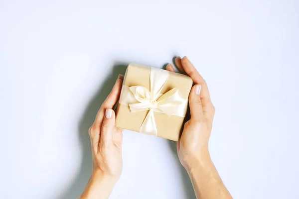 Primer plano de las manos femeninas sosteniendo regalo de cumpleaños en envoltura de papel artesanal vintage. Composición femenina con presente en los brazos de la mujer . — Foto de Stock