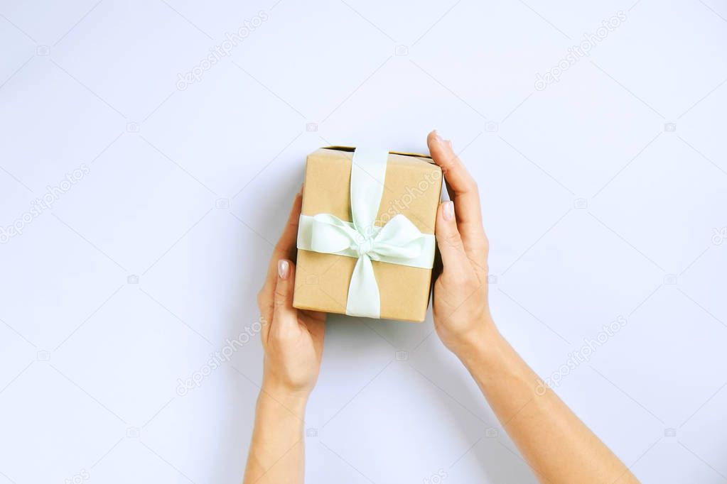 Close up of female hands holding birthday gift in vintage craft paper wrapping. Femenine composition with present in woman's arms.