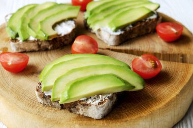 Vejetaryen sandviç, çavdar ekmeği tost, avokado, kiraz domates, vegenaise eggless mayonez sos kalın kırık ahşap dilim, Beyaz ahşap doku masada. Ulusal avokado gün kavramı. Yakın çekim, arka plan.