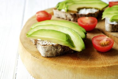 Vejetaryen sandviç, çavdar ekmeği tost, avokado, kiraz domates, vegenaise eggless mayonez sos kalın kırık ahşap dilim, Beyaz ahşap doku masada. Ulusal avokado gün kavramı. Yakın çekim, arka plan.