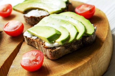Vejetaryen sandviç, çavdar ekmeği tost, avokado, kiraz domates, vegenaise eggless mayonez sos kalın kırık ahşap dilim, Beyaz ahşap doku masada. Ulusal avokado gün kavramı. Yakın çekim, arka plan.