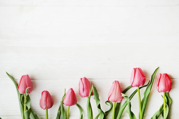 Bunch of pink tulip in beautiful spring holidays composition lying on white wooden textured table background. Mother's day bouquet arrangement. Flowers for women's day. Copy space, close up, top view. — Stock Photo, Image
