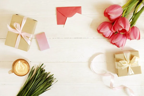 Composição feminina do espaço de trabalho da mulher w / cartão de saudação em branco, envolope & presentes para o dia da mãe. Xícara de café com arte latte & tulipa flowe bouquet. Espaço de cópia, flat lay, fundo, vista superior . — Fotografia de Stock