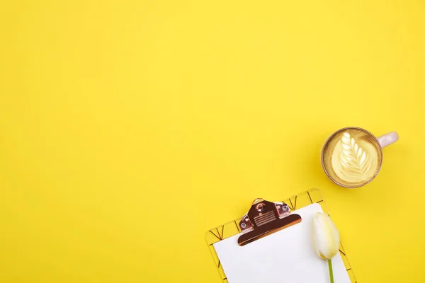 Composición femenina de escritorio con portapapeles en blanco, lápiz, taza de café, ramo de tulipanes sobre fondo amarillo. Trabajo femenino, flores para el día de la madre. Vista superior, plano, primer plano, espacio para copiar . — Foto de Stock