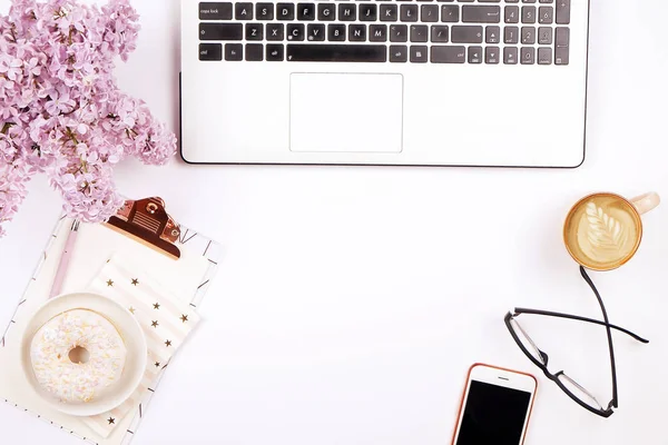 Draufsicht auf den Schreibtisch einer Arbeiterin mit Laptop, Blumen und verschiedenen Büroutensilien. feminine kreative Gestaltung. — Stockfoto