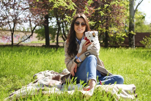 Portret atrakcyjna młoda kobieta, przytulanie Śliczne jack russell Terier szczeniak w parku, zielony trawnik tło liści. Hipster Kobieta w okulary, uśmiechnięty, zwierzęta jej psa na trawie. Bliska, kopiować miejsca. — Zdjęcie stockowe