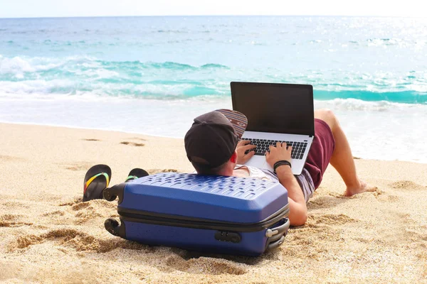 Młody człowiek w rękawów, szorty, cap snapback plaży z laptopa & walizkę. Freelancer, hipster bloger, pisarz, ciesząc się widokiem na morze — Zdjęcie stockowe