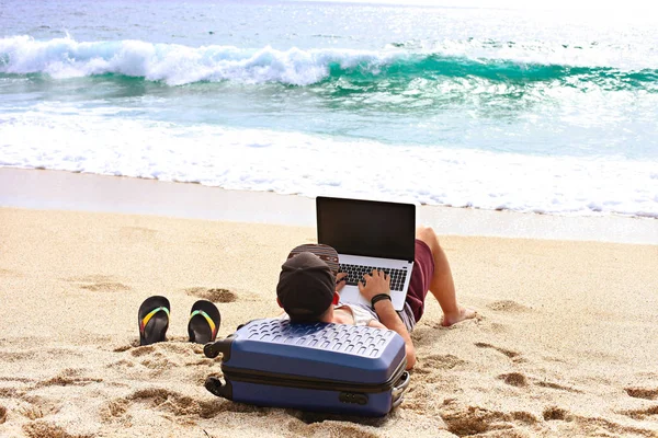 Młody człowiek w rękawów, szorty, cap snapback plaży z laptopa & walizkę. Freelancer, hipster bloger, pisarz, ciesząc się widokiem na morze — Zdjęcie stockowe