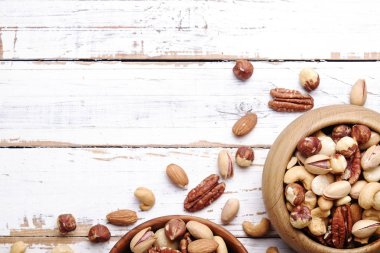 Geride çizilmiş Beyaz ahşap masa arka plan, yumuşak yaz üzerinde kahverengi ahşap kase fındık çeşitleri ile karıştırın. Kopya alanı.