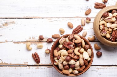 Geride çizilmiş Beyaz ahşap masa arka plan, yumuşak yaz üzerinde kahverengi ahşap kase fındık çeşitleri ile karıştırın. Kopya alanı.