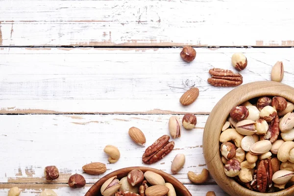 Geride çizilmiş Beyaz ahşap masa arka plan, yumuşak yaz üzerinde kahverengi ahşap kase fındık çeşitleri ile karıştırın. Kopya alanı.