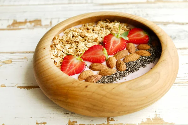 Wooden smoothie bowl, assorted ingredients on table. Healthy nutritious breakfast with vegan yogurt, raw fruits, nuts and cereals. — Stock Photo, Image