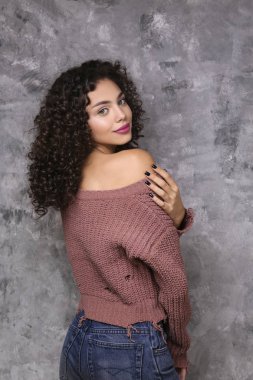 Hafif makyajlı, kıvırcık saçlı, sıkıntılı bir süveter giyen güzel bir kadın..