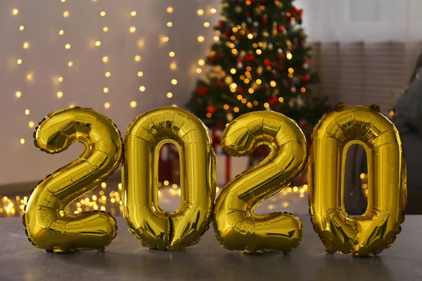 Traditional christmas pine tree with holiday decorations on background and 2020 shaped balloons on foreground. Bokeh lights glowing in the evening. Close up, copy space, background, interior.