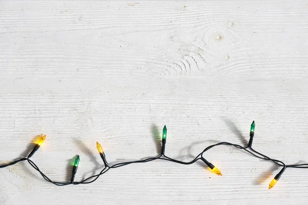 Concetto di sfondo natalizio. Le luci di decorazione di anno nuovo, la ghirlanda con molte piccole lampade di colore diverso brillano su tavolo di legno grunged grigio. Vista dall'alto, disposizione piatta, spazio di copia . — Foto Stock