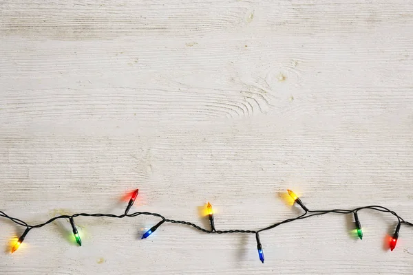 Concepto de fondo de Navidad. Las luces de decoración de año nuevo, guirnalda con muchas lámparas pequeñas de diferentes colores brillan en la mesa de madera gris gruesa. Vista superior, plano, espacio para copiar . — Foto de Stock