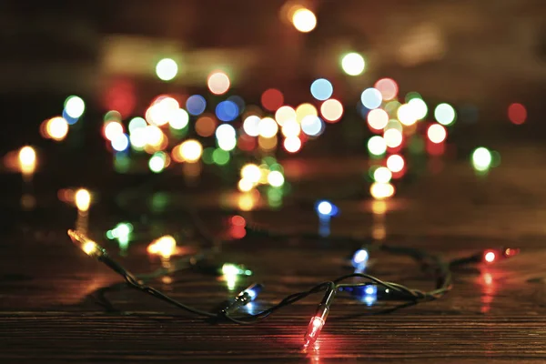 Concetto di sfondo natalizio. Le luci di decorazione di anno nuovo, la ghirlanda con molte piccole lampade di colore diverso brillano su tavolo di legno grunged marrone. Vista dall'alto, disposizione piatta, spazio di copia . — Foto Stock