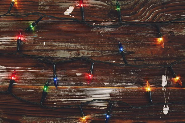 Concetto di sfondo natalizio. Le luci di decorazione di anno nuovo, la ghirlanda con molte piccole lampade di colore diverso brillano su tavolo di legno grunged marrone. Vista dall'alto, disposizione piatta, spazio di copia . — Foto Stock