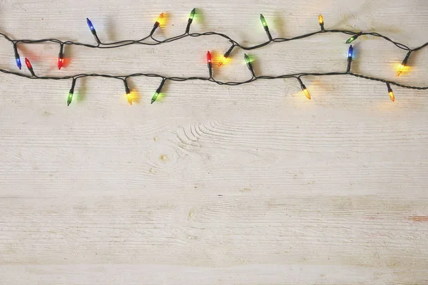 Concetto di sfondo natalizio. Le luci di decorazione di anno nuovo, la ghirlanda con molte piccole lampade di colore diverso brillano su tavolo di legno grunged grigio. Vista dall'alto, disposizione piatta, spazio di copia . — Foto Stock