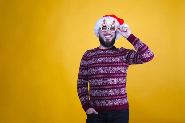 在工作室里，英俊的大胡子男子身穿圣诞毛衣，头戴雪花装饰的圣诞饰物，头戴圣诞礼帽，站在黄色的墙壁上，模仿空间。 节日背景。 满脸笑容的男人. — 图库照片