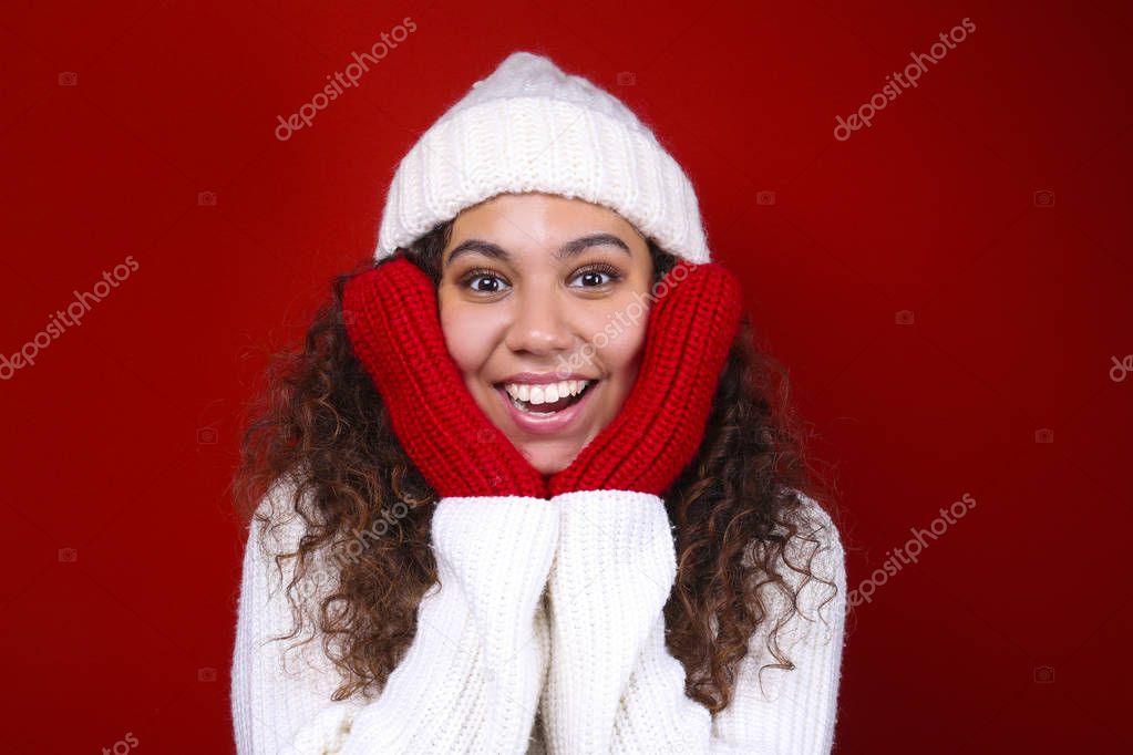Studio portrait of young woman with dark skin and long curly hair wearing knitted turtle neck sweater over the festive red wall with a lot of copy space for text. Close up, isolated background.