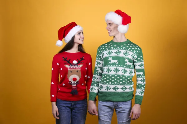 Un par de jóvenes vistiendo suéteres feos de Navidad, posando sobre un colorido fondo aislado . — Foto de Stock