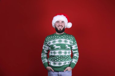 Kırmızı duvar arkasında, Noel kıyafetiyle sakallı genç bir adam..