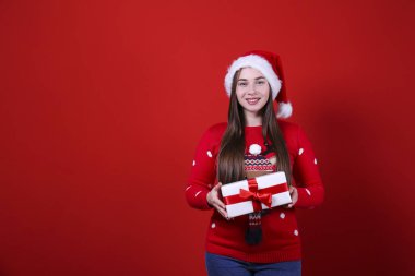 Kırmızı duvarda Noel Baba şapkası takan gülümseyen bir kadın..